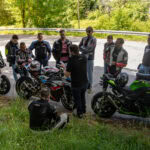 Gruppo di motociclisti che ascolta istruzioni con moto sportive e da turismo in un'area verde.