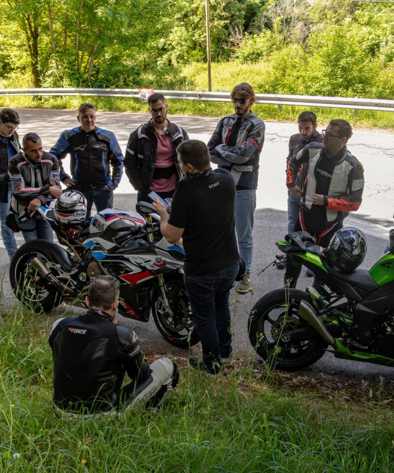 Gruppo di motociclisti che ascolta istruzioni con moto sportive e da turismo in un'area verde.